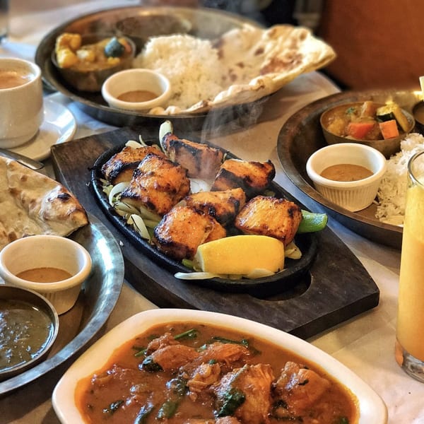 A table laden with various Nepalese dishes, including steaming grilled chicken, curries, rice, and naan.