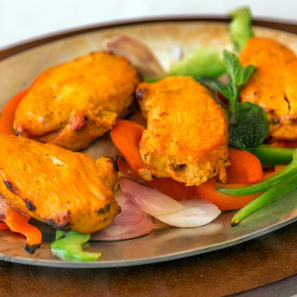 Four pieces of Nepalese chicken tikka with bell peppers, onions, and mint on a metal plate.