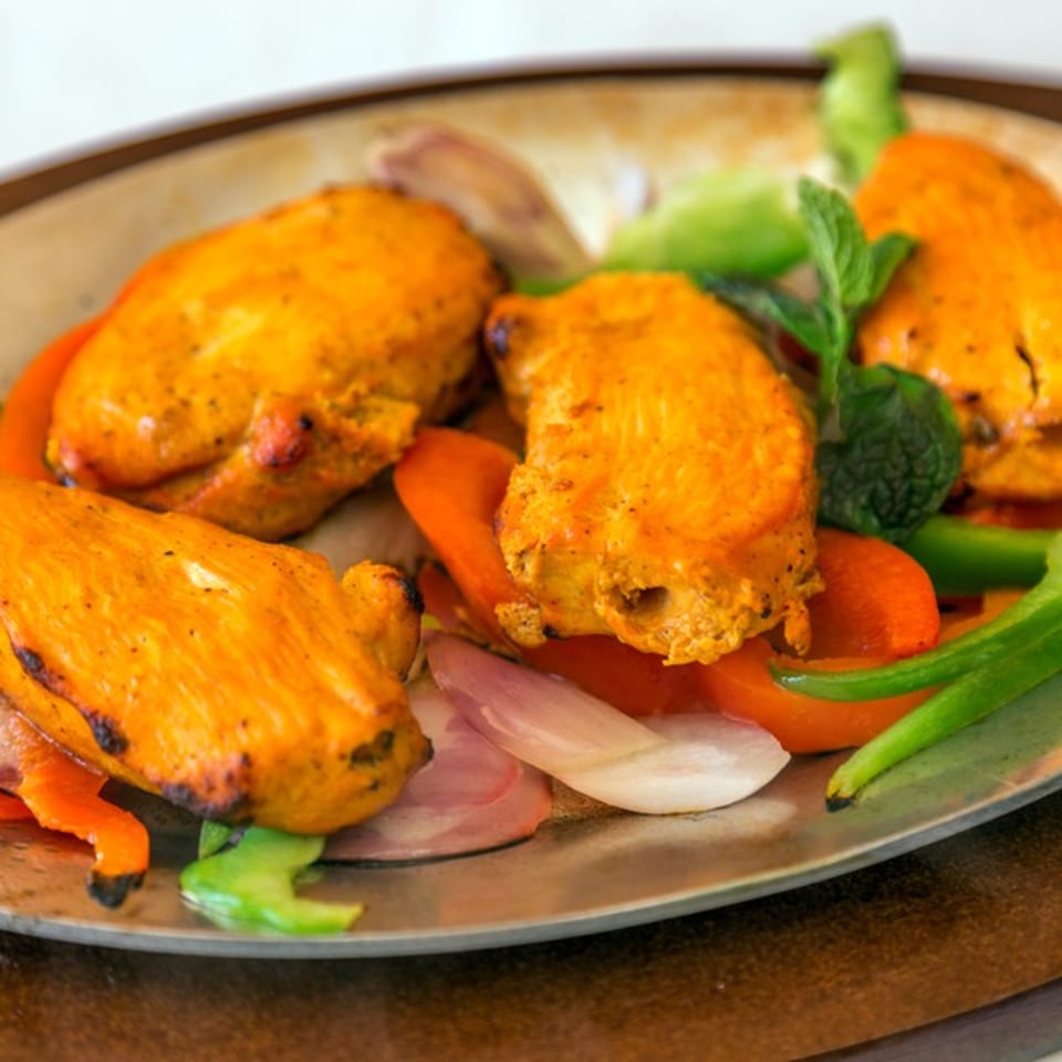 Four pieces of Nepalese chicken tikka with bell peppers, onions, and mint on a metal plate.