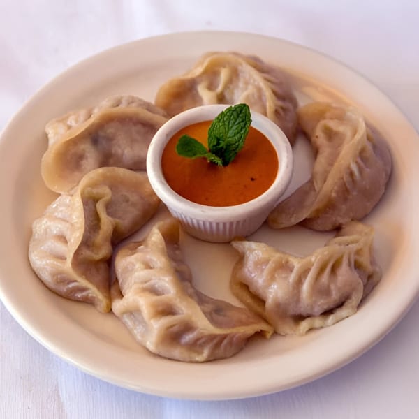 A plate of Nepalese momo dumplings with a small bowl of orange dipping sauce garnished with mint.