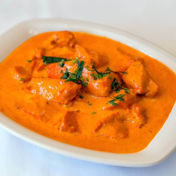 Nepalese chicken curry in a rich orange sauce, garnished with fresh green herbs in a white dish.