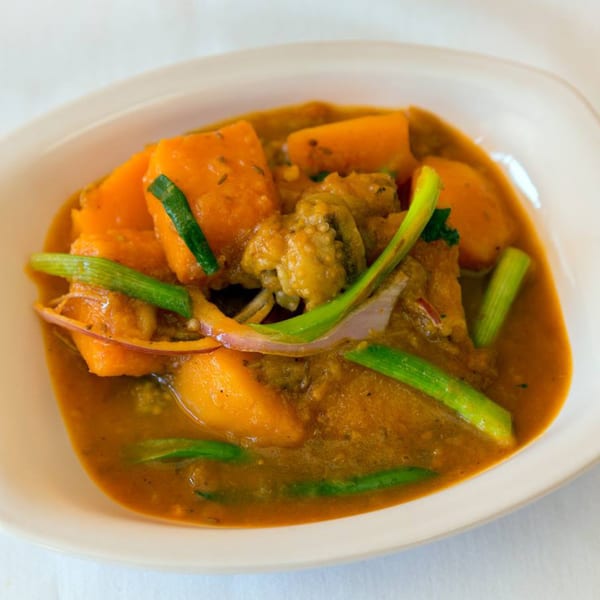 A bowl of Nepalese chicken curry with large pieces of pumpkin and green onions.
