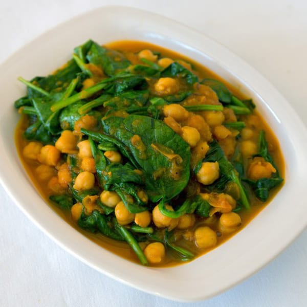 A white oval dish filled with Nepalese chickpea and spinach curry in a rich orange sauce.