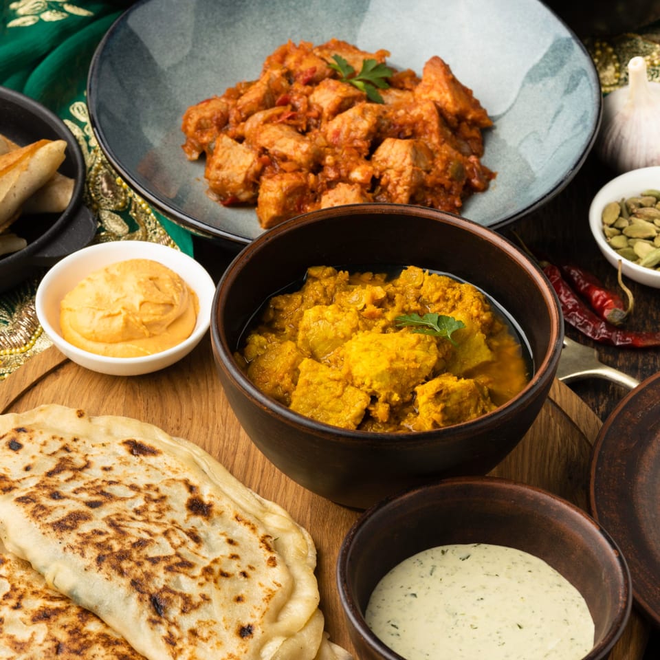 A close-up of various Nepalese dishes, including curries, flatbread, and dipping sauces, on a wooden board.