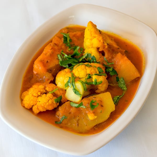 Aloo Gobi, a Nepalese dish with cauliflower and potatoes in a rich orange sauce, garnished with cilantro.