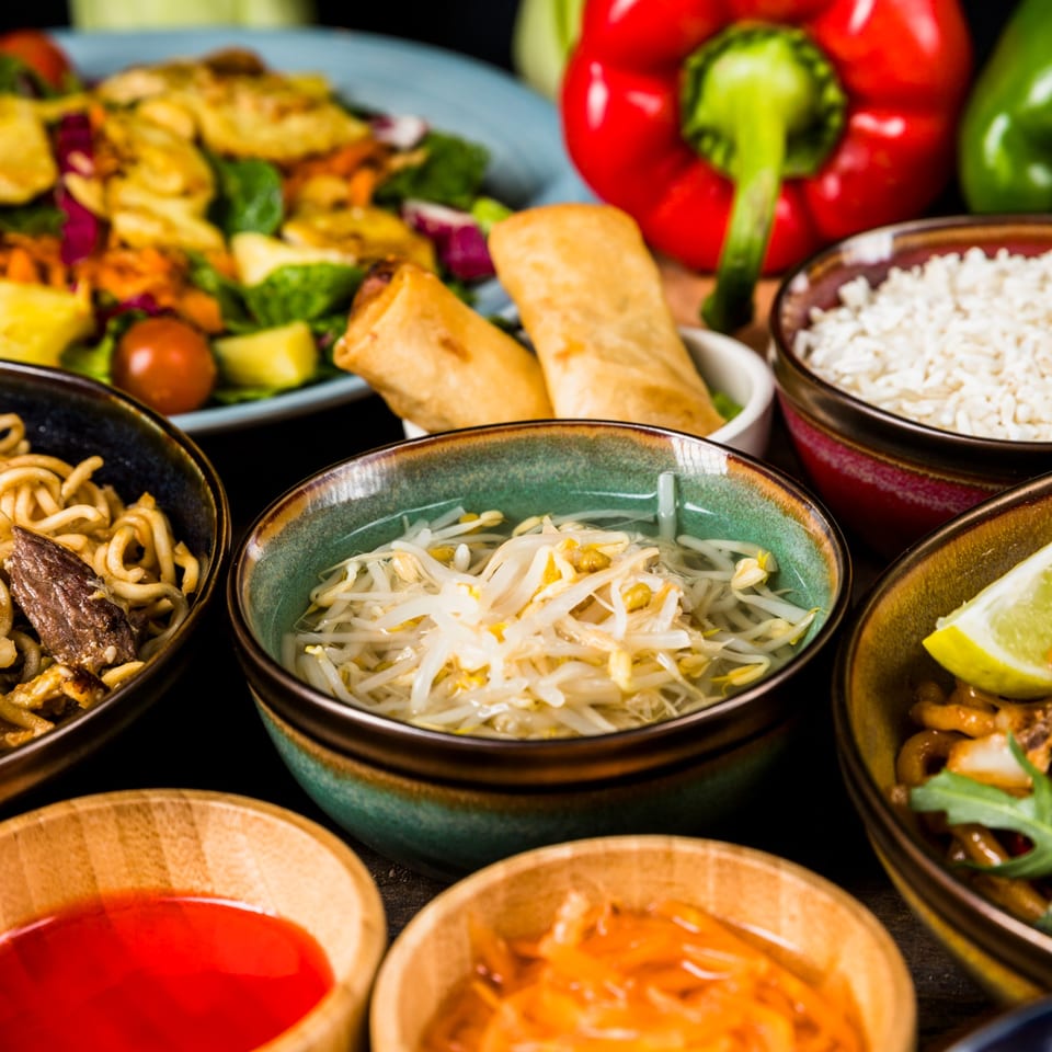 A vibrant spread of Nepalese dishes, including noodles, rice, spring rolls, and fresh vegetables.