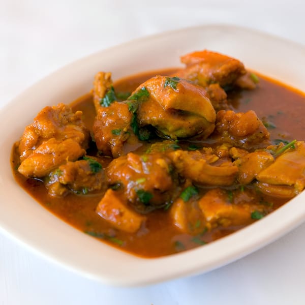 Close-up of a vibrant Nepalese chicken curry with rich orange sauce and green herbs in a white bowl.