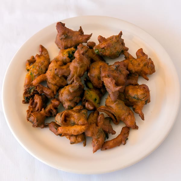 A white plate filled with golden-brown, irregularly shaped Nepalese vegetable pakoras or fritters.