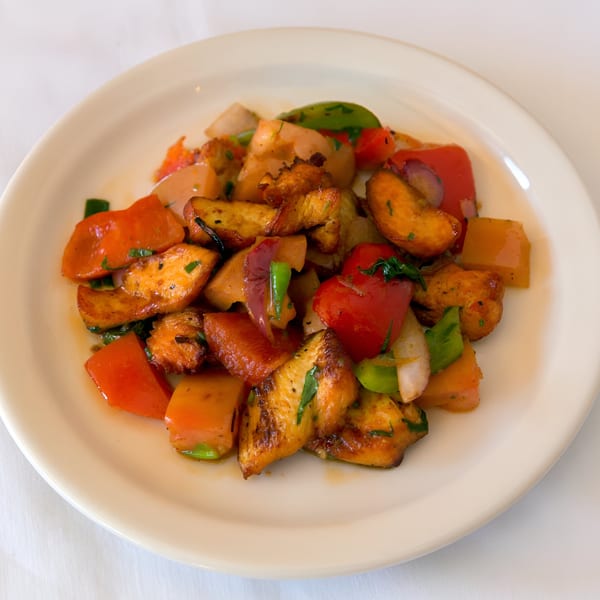 Close-up of a Nepalese dish with sautéed chicken, red bell peppers, onions, and herbs on a white plate.