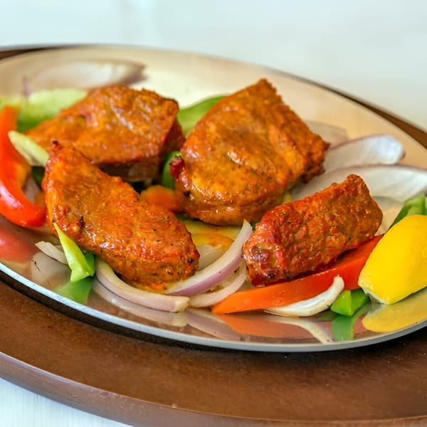 Nepalese chicken tikka with bell peppers, onions, and lemon wedges on a silver platter.