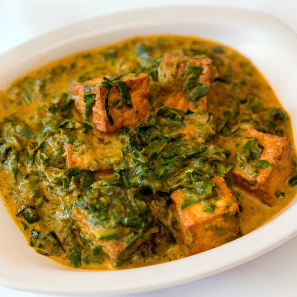 Close-up of a white bowl filled with Nepalese palak paneer, featuring golden paneer cubes in a creamy spinach sauce.