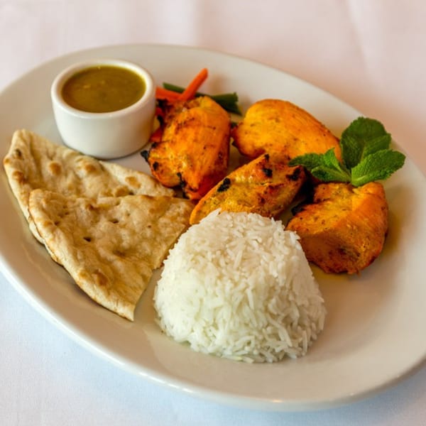 Nepalese chicken tikka with rice, naan bread, and a side of sauce on a white plate.